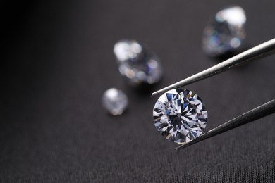 Photo of Tweezers with beautiful shiny diamonds on black fabric, closeup