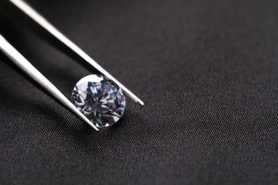 Photo of Tweezers with beautiful shiny diamond on black fabric, closeup. Space for text