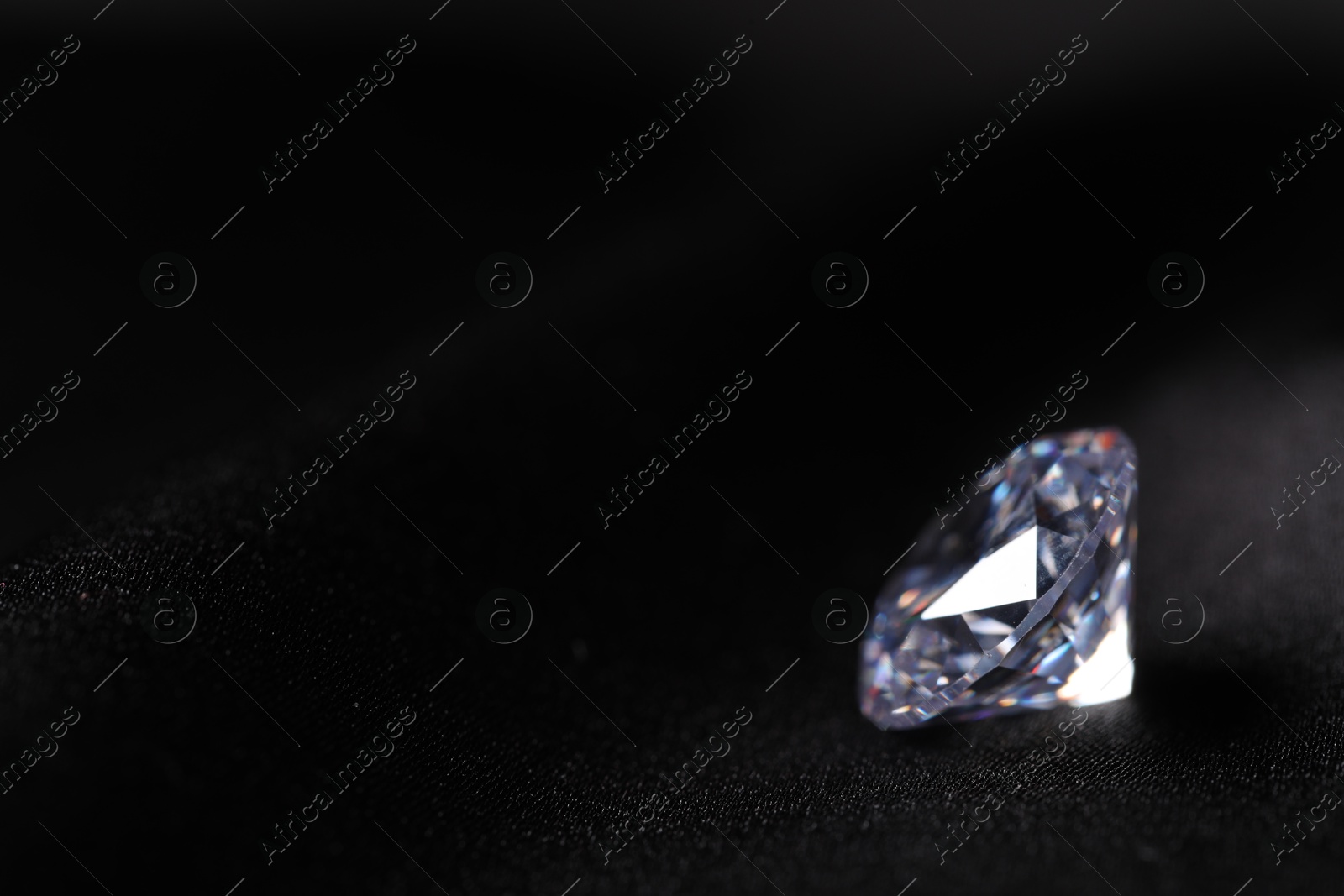 Photo of One beautiful shiny diamond on black fabric, closeup. Space for text