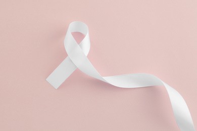 Photo of White awareness ribbon on beige background, top view
