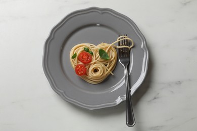 Photo of Heart made of tasty spaghetti, fork, tomato and basil on white marble table, top view