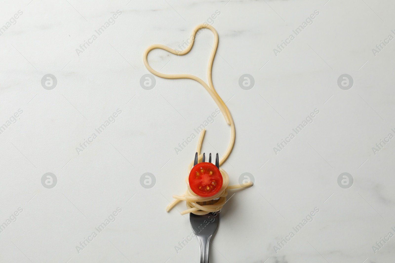 Photo of Heart made of tasty spaghetti, fork and tomato on white marble table, top view