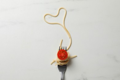 Photo of Heart made of tasty spaghetti, fork and tomato on white marble table, top view