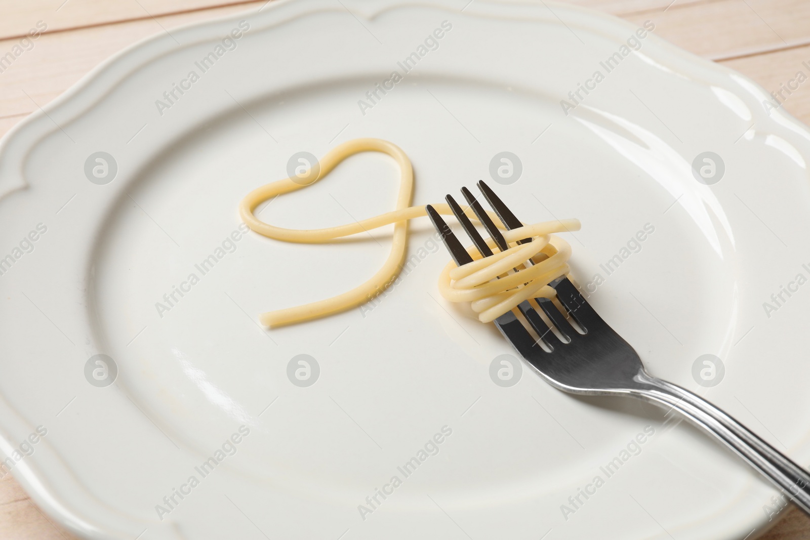 Photo of Heart made of tasty spaghetti and fork on table, closeup