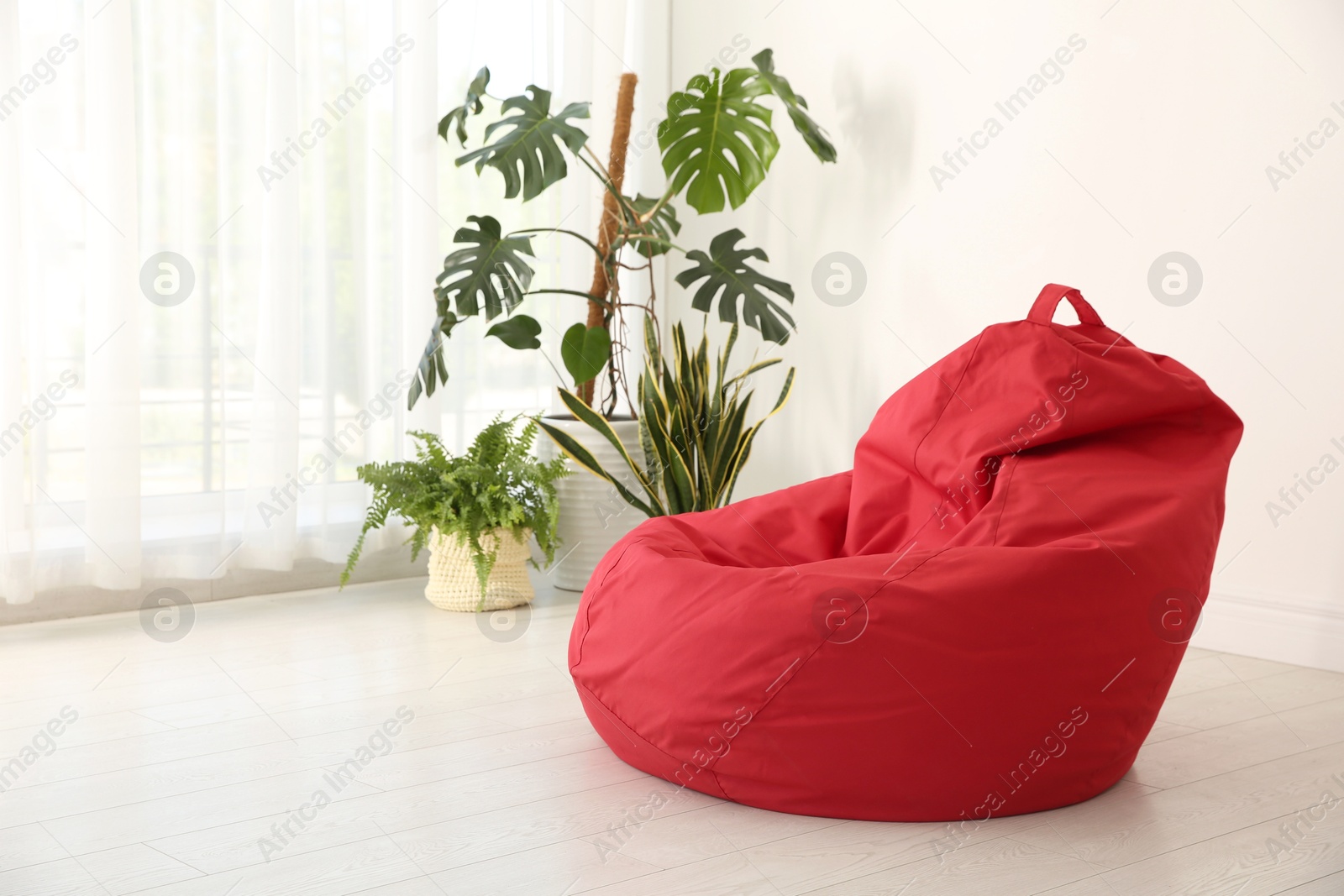 Photo of Red bean bag chair near light wall in room. Space for text