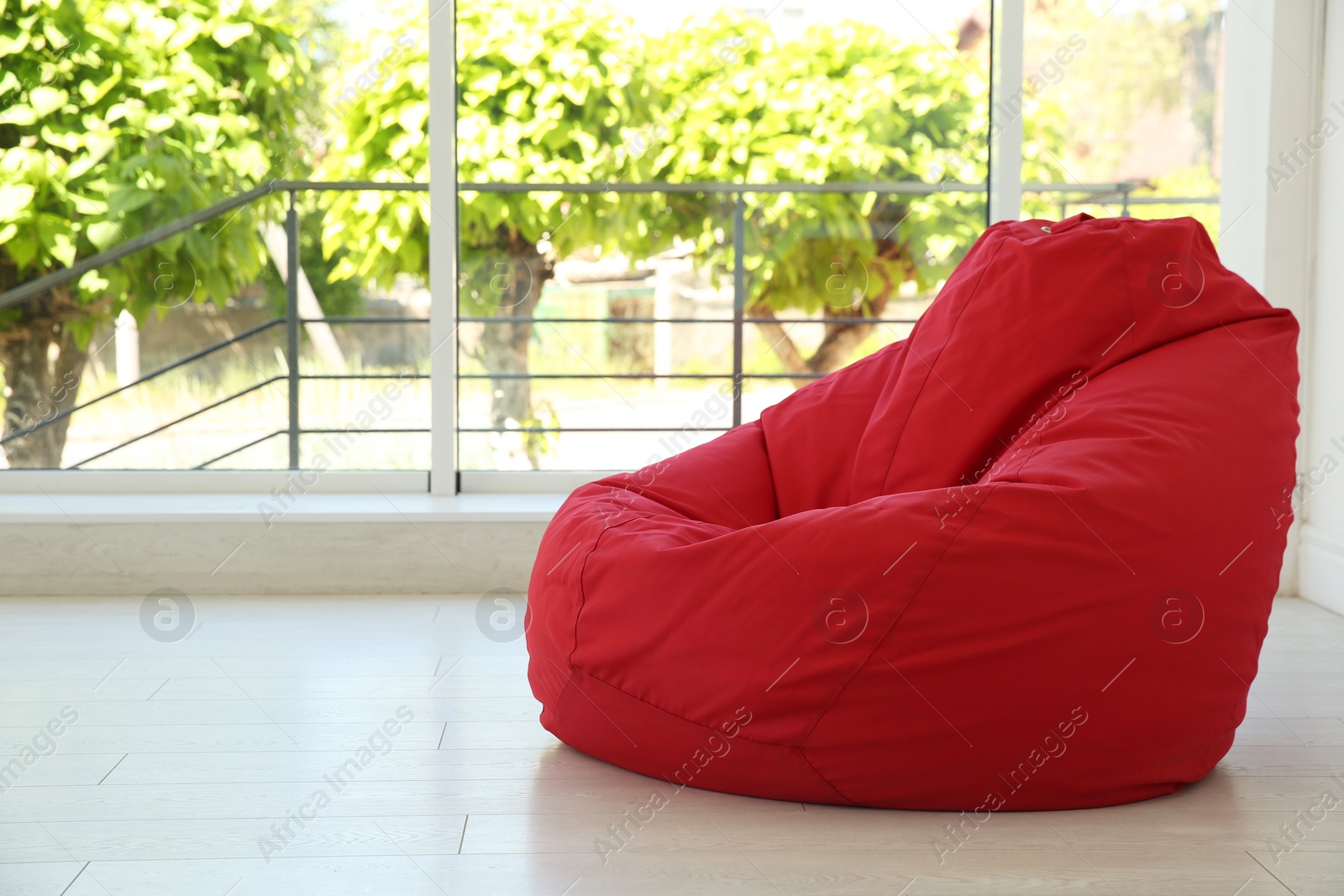 Photo of Red bean bag chair near window in room. Space for text