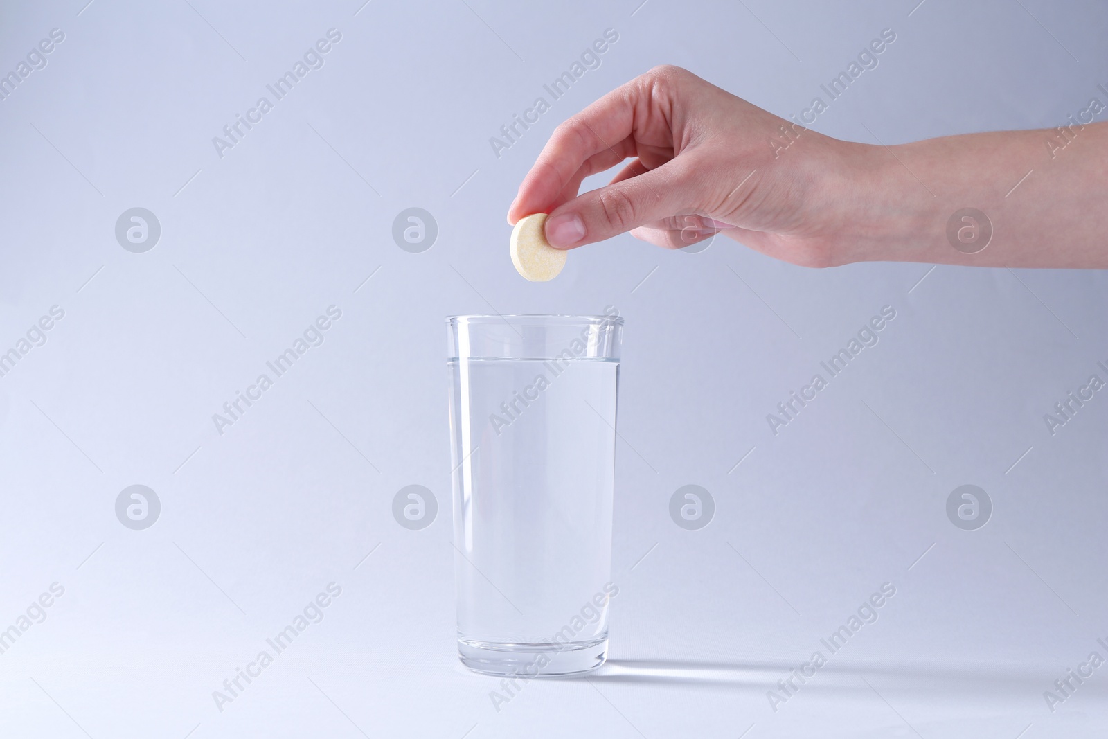 Photo of Woman putting effervescent pill into glass of water on light grey background, closeup