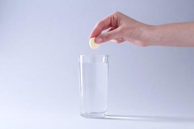 Photo of Woman putting effervescent pill into glass of water on light grey background, closeup