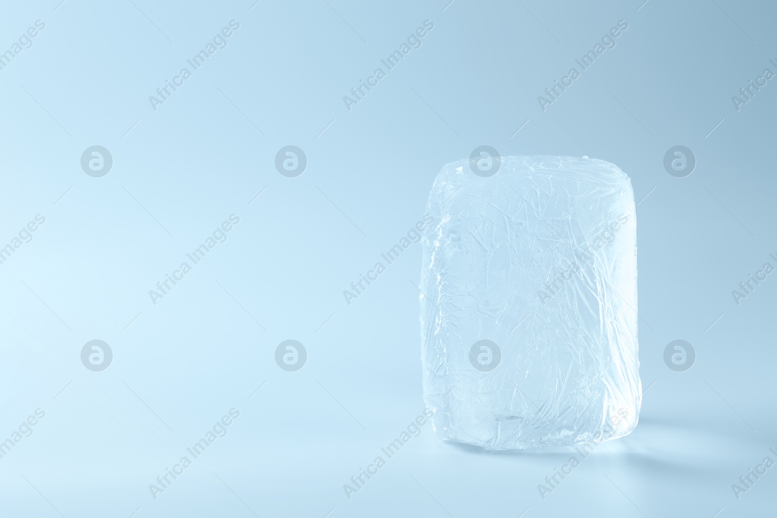 Photo of Block of clear ice on light blue background, space for text