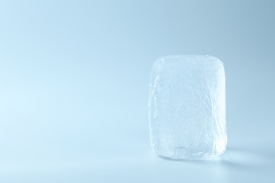 Photo of Block of clear ice on light blue background, space for text