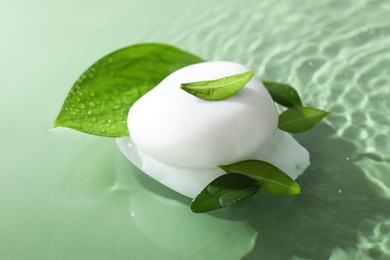 Photo of Spa stones and fresh leaves in water on light green background, closeup