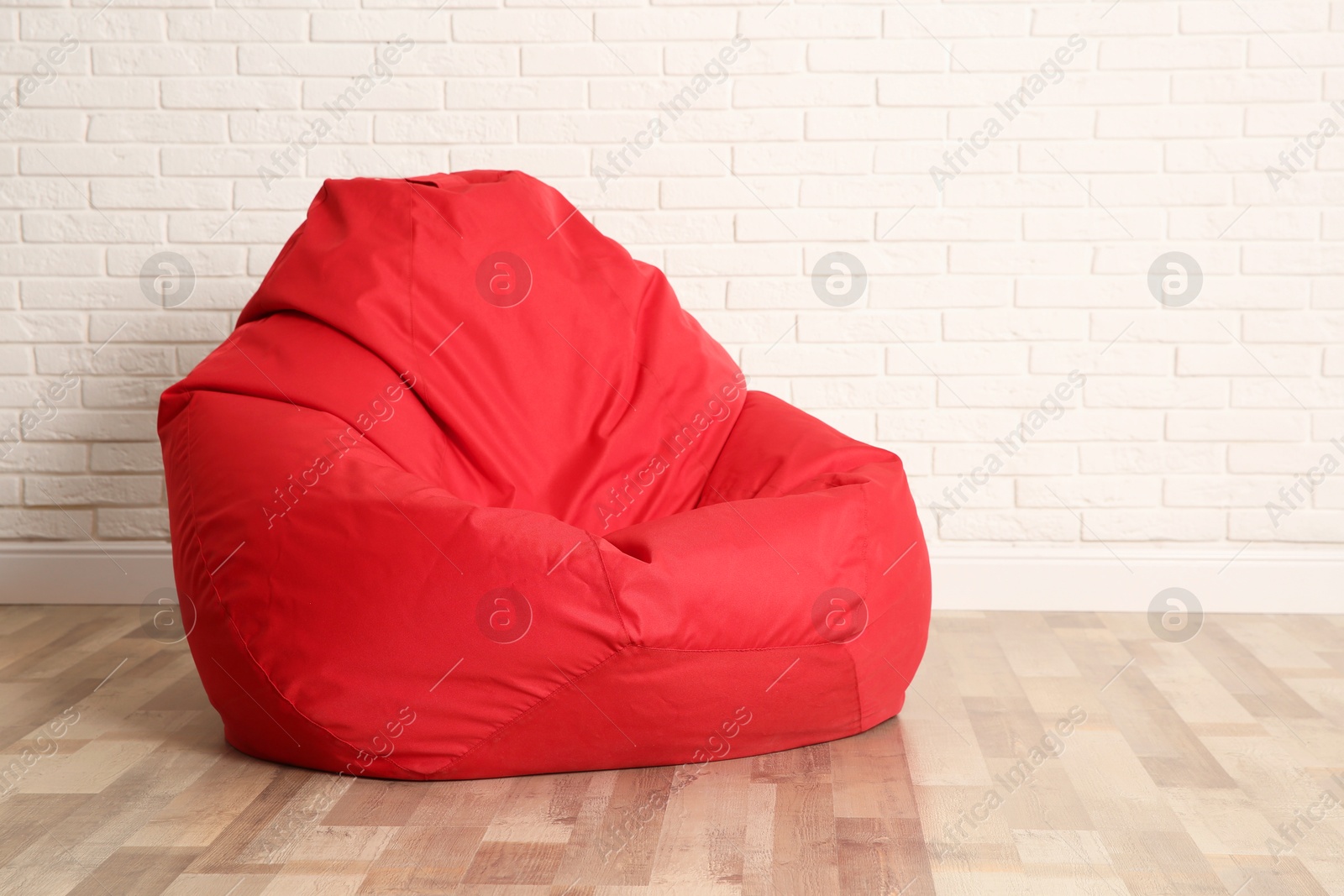 Photo of Red bean bag chair near white brick wall in room. Space for text