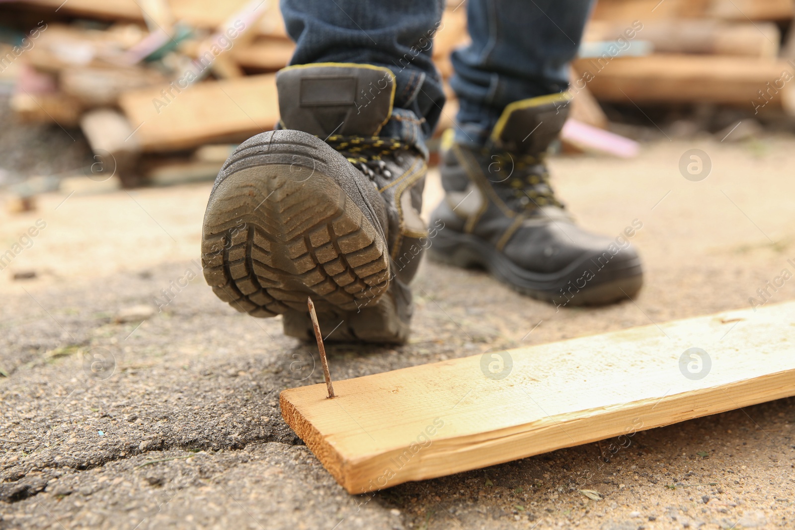 Photo of Careless worker stepping on nail in wooden plank outdoors, closeup