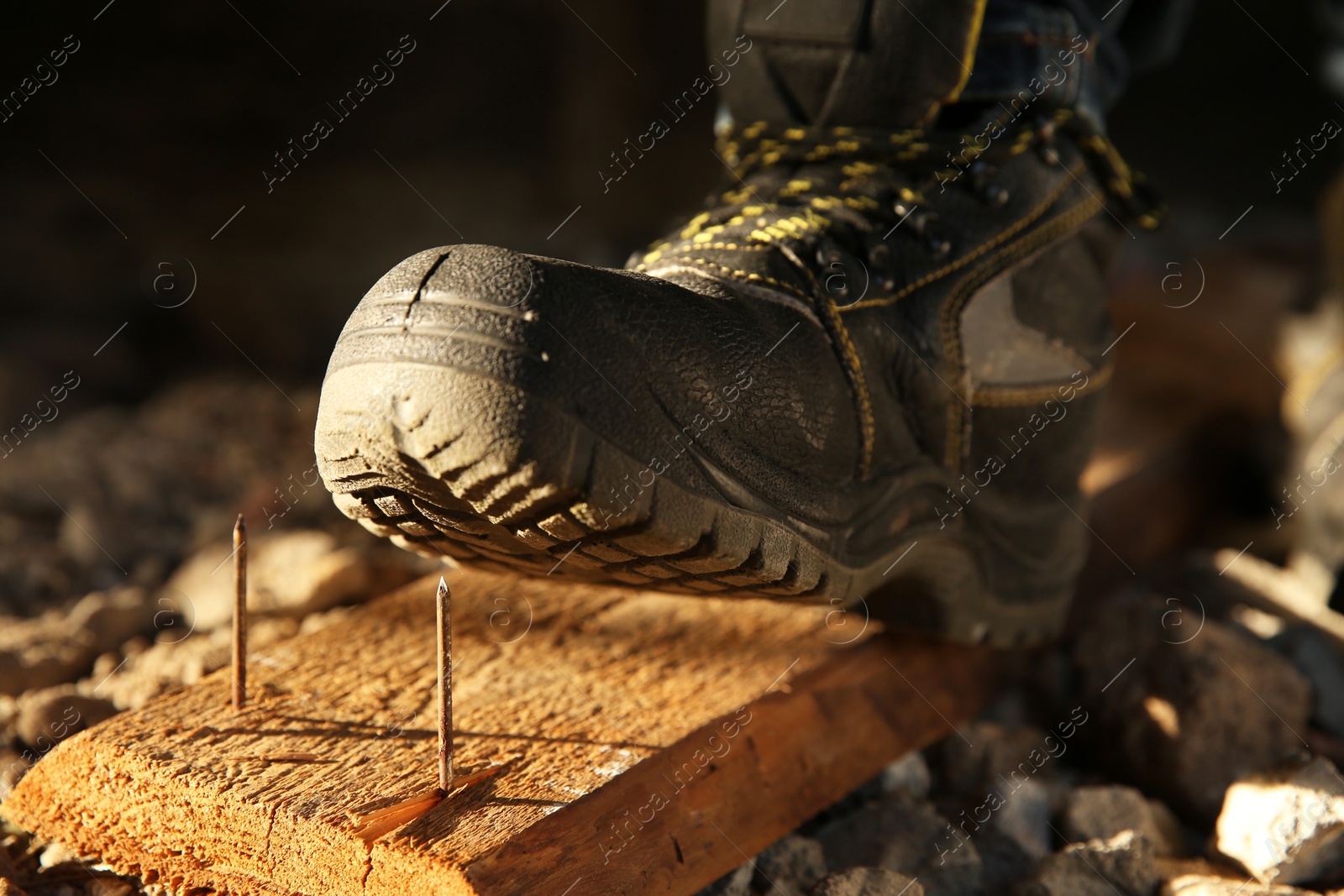 Photo of Careless worker stepping on nails in wooden plank, closeup