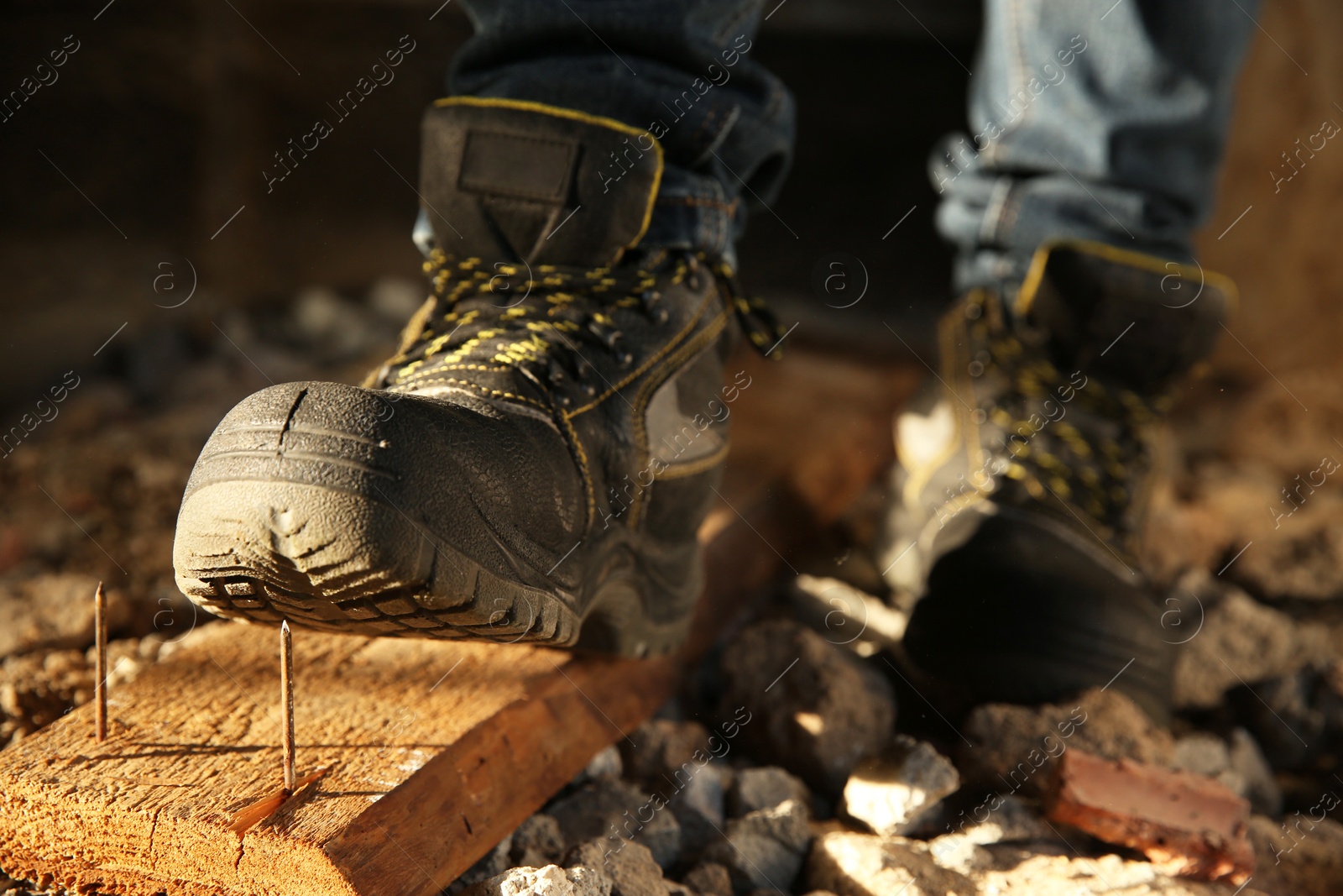 Photo of Careless worker stepping on nails in wooden plank, closeup