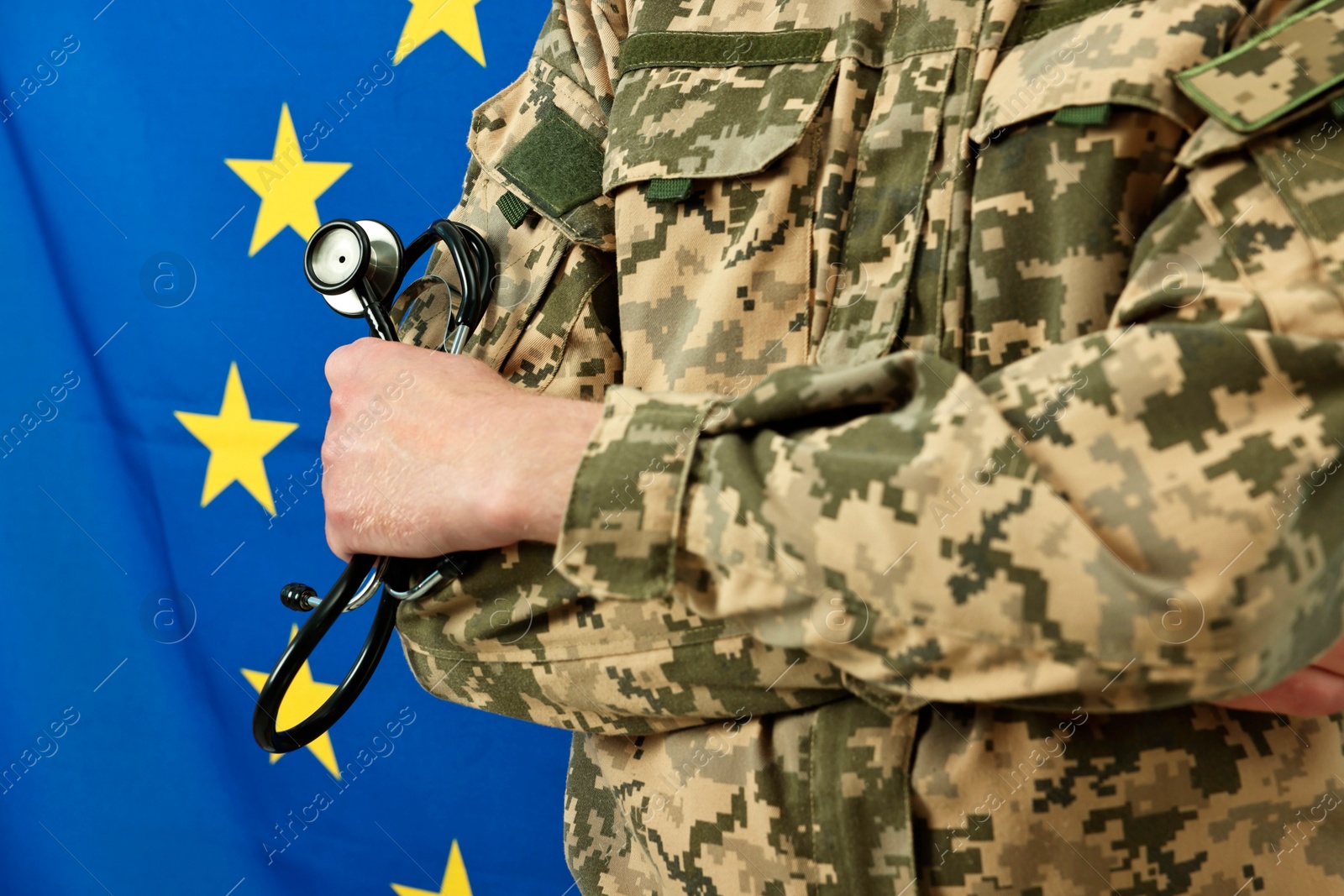 Photo of Man in military uniform with crossed arms and stethoscope against flag of European Union, closeup. Health care concept