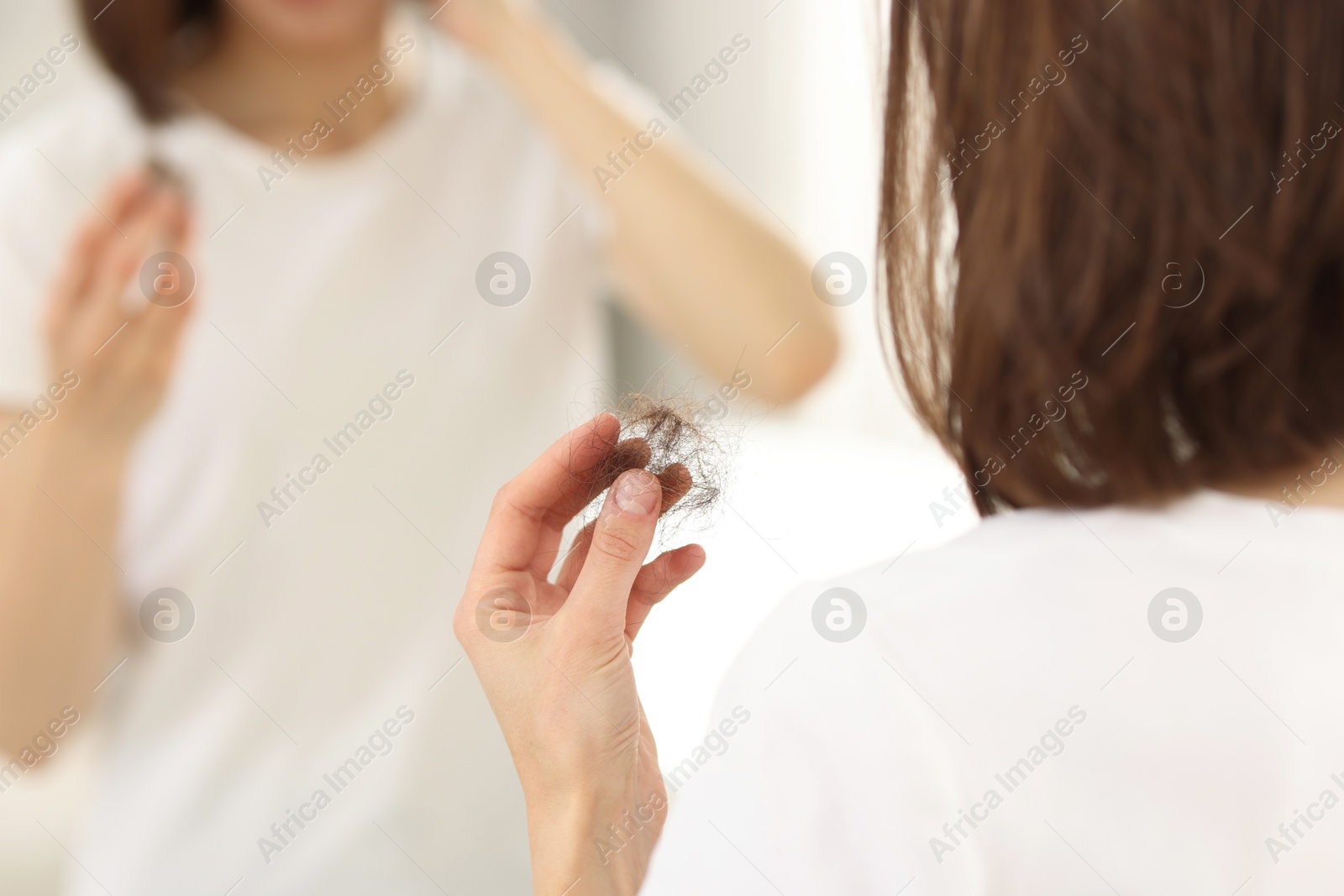 Photo of Woman holding clump of lost hair near mirror indoors, closeup. Alopecia problem