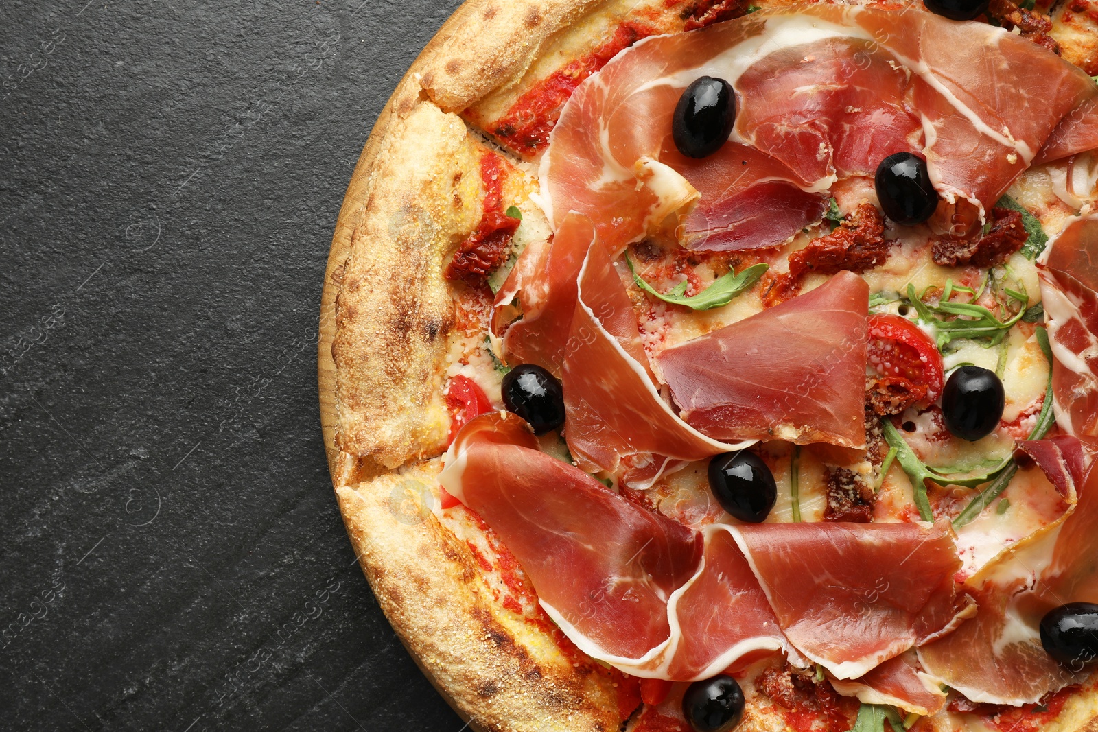 Photo of Tasty pizza with cured ham, olives and sun-dried tomato on black table, top view. Space for text