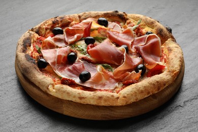 Photo of Tasty pizza with cured ham, olives and sun-dried tomato on black table