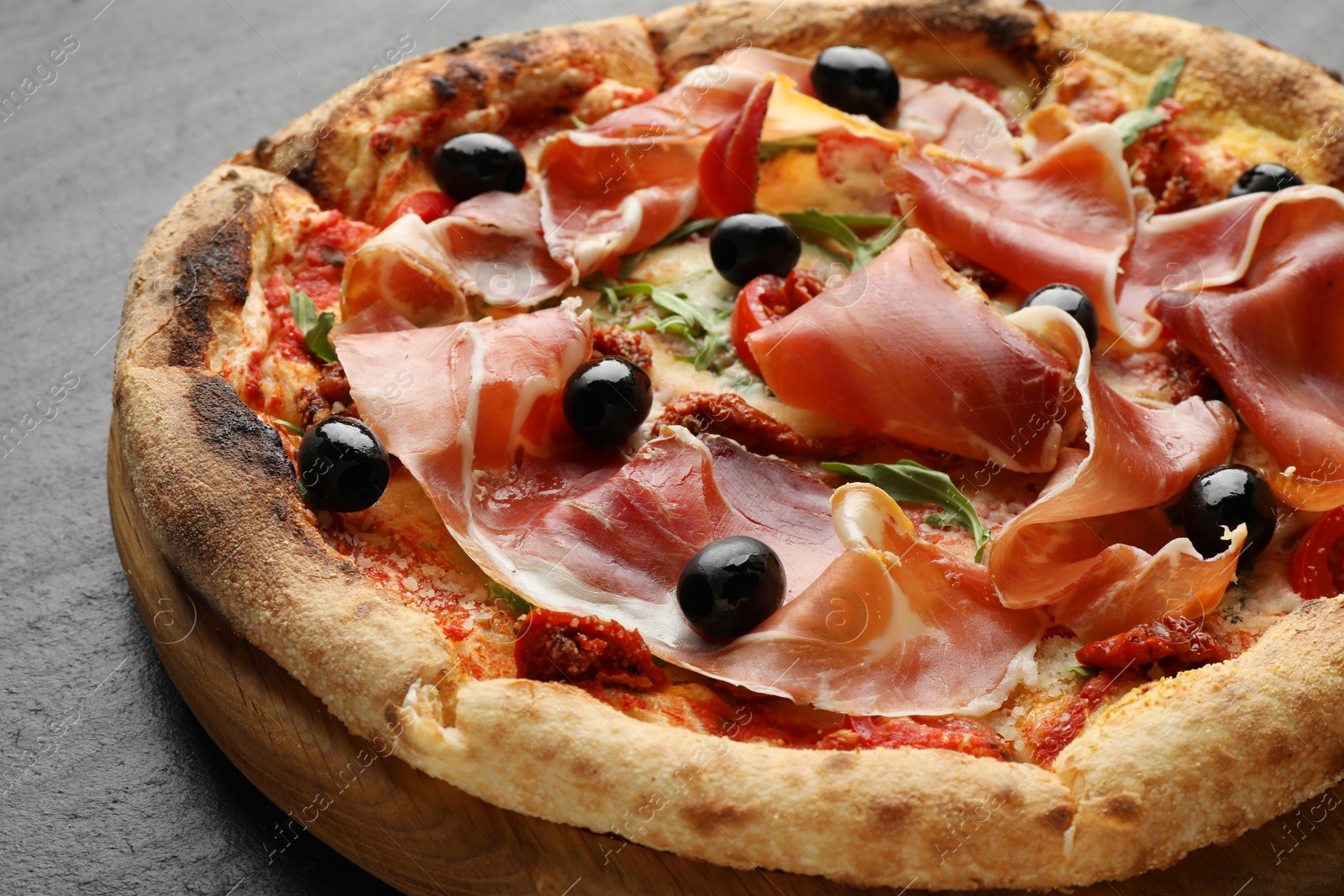 Photo of Tasty pizza with cured ham, olives and sun-dried tomato on black table, closeup