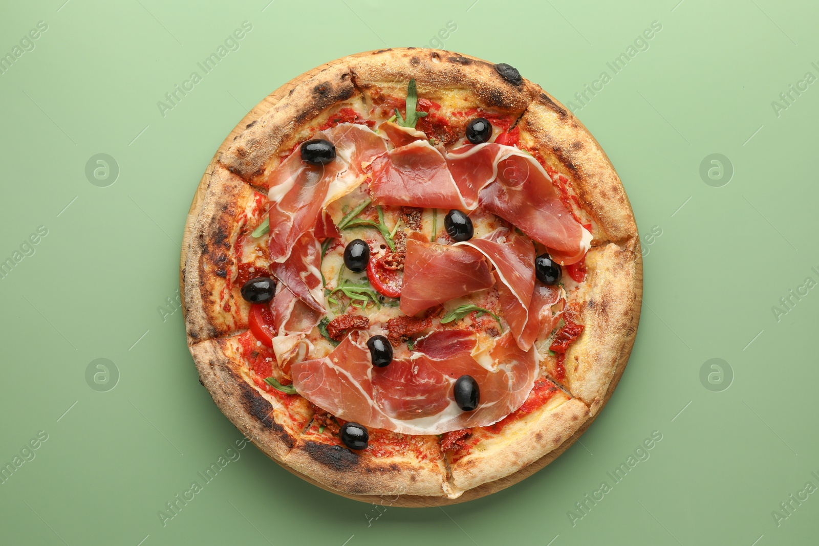 Photo of Tasty pizza with cured ham, olives and sun-dried tomato on green background, top view