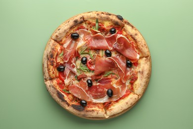 Tasty pizza with cured ham, olives and sun-dried tomato on green background, top view