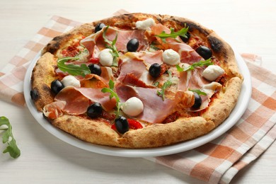 Photo of Tasty pizza with cured ham, olives, mozzarella cheese, sun-dried tomato and arugula on light wooden table