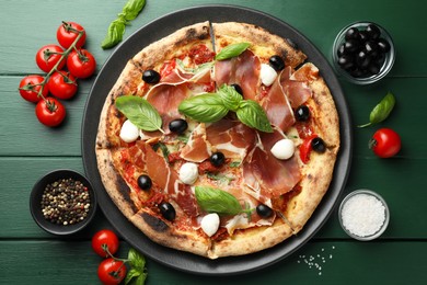 Photo of Tasty pizza with cured ham, olives, mozzarella cheese, tomatoes and arugula on green wooden table, flat lay