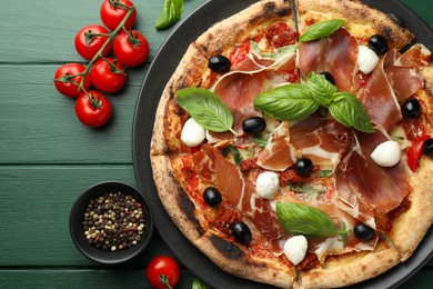 Photo of Tasty pizza with cured ham, olives, mozzarella cheese, tomatoes and arugula on green wooden table, flat lay