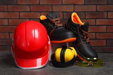 Photo of Pair of working boots, hard hat, protective goggles and earmuffs on grey surface