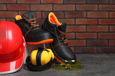 Photo of Pair of working boots, hard hat, protective goggles and earmuffs on grey surface. Space for text
