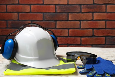 Photo of Hard hat, earmuffs, gloves, protective goggles and reflective vest on white wooden surface
