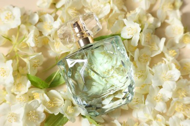 Photo of Bottle of aromatic perfume among jasmine flowers on beige background, flat lay