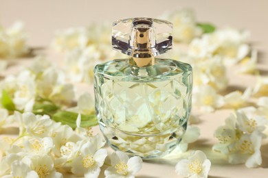 Photo of Bottle of aromatic perfume and jasmine flowers on beige background, closeup