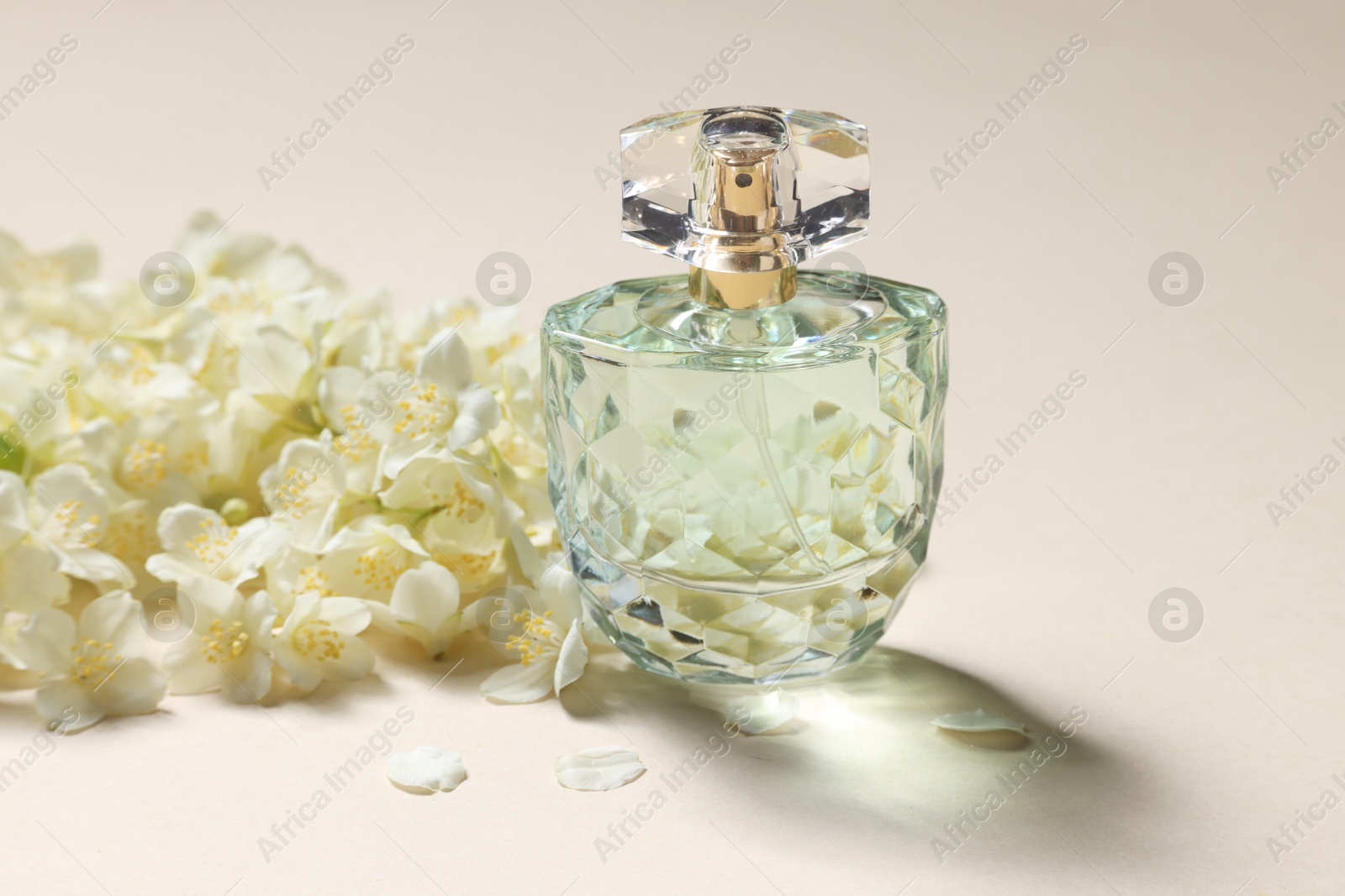 Photo of Bottle of aromatic perfume and jasmine flowers on beige background, closeup