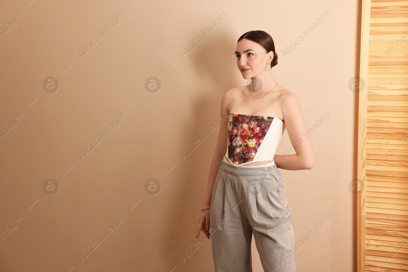 Photo of Beautiful young woman in stylish corset near beige wall, space for text