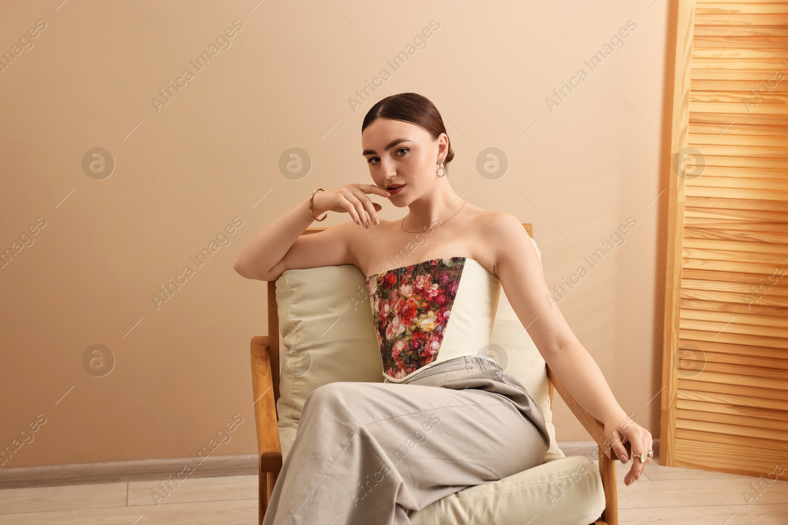 Photo of Beautiful young woman in stylish corset on armchair indoors