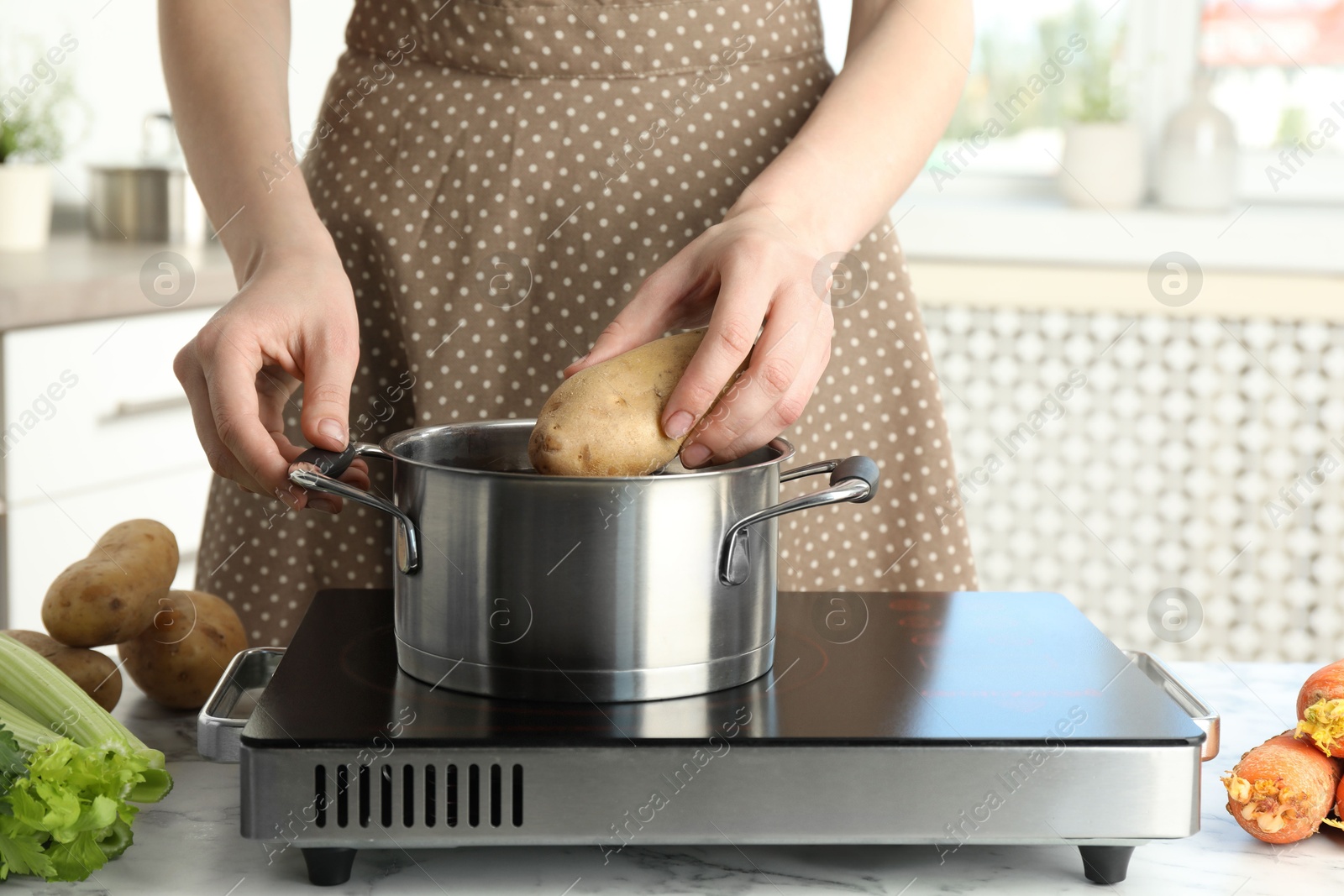 Photo of Woman putting potato into metal pot on stove, closeup