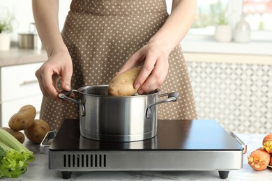 Woman putting potato into metal pot on stove, closeup