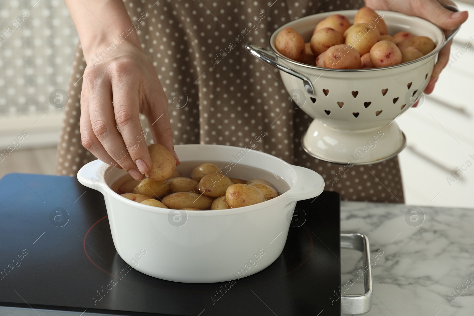 Photo of Woman putting potato into metal pot on stove, closeup