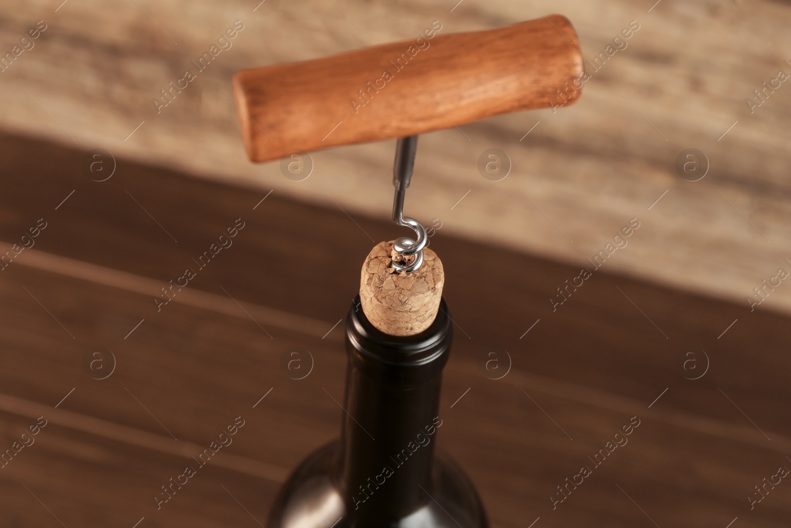 Photo of Wine bottle with corkscrew on wooden background, closeup