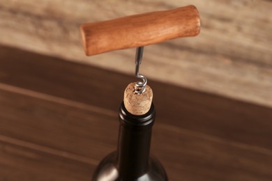 Photo of Wine bottle with corkscrew on wooden background, closeup