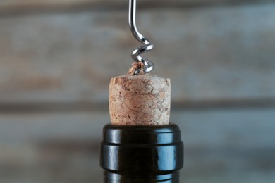 Photo of Wine bottle with corkscrew on blurred background, closeup