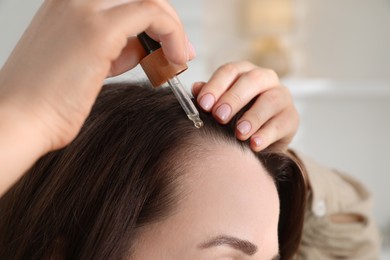 Photo of Hair loss problem. Woman applying serum onto hairline indoors, closeup