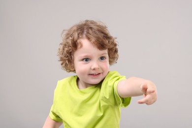 Photo of Portrait of cute little boy pointing at something on grey background