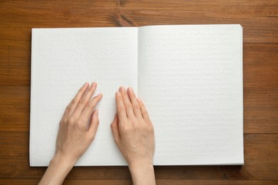 Photo of Blind woman reading book written in Braille at wooden table, top view