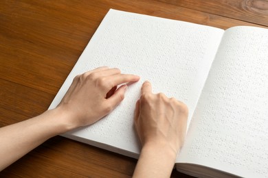 Blind woman reading book written in Braille at wooden table, closeup