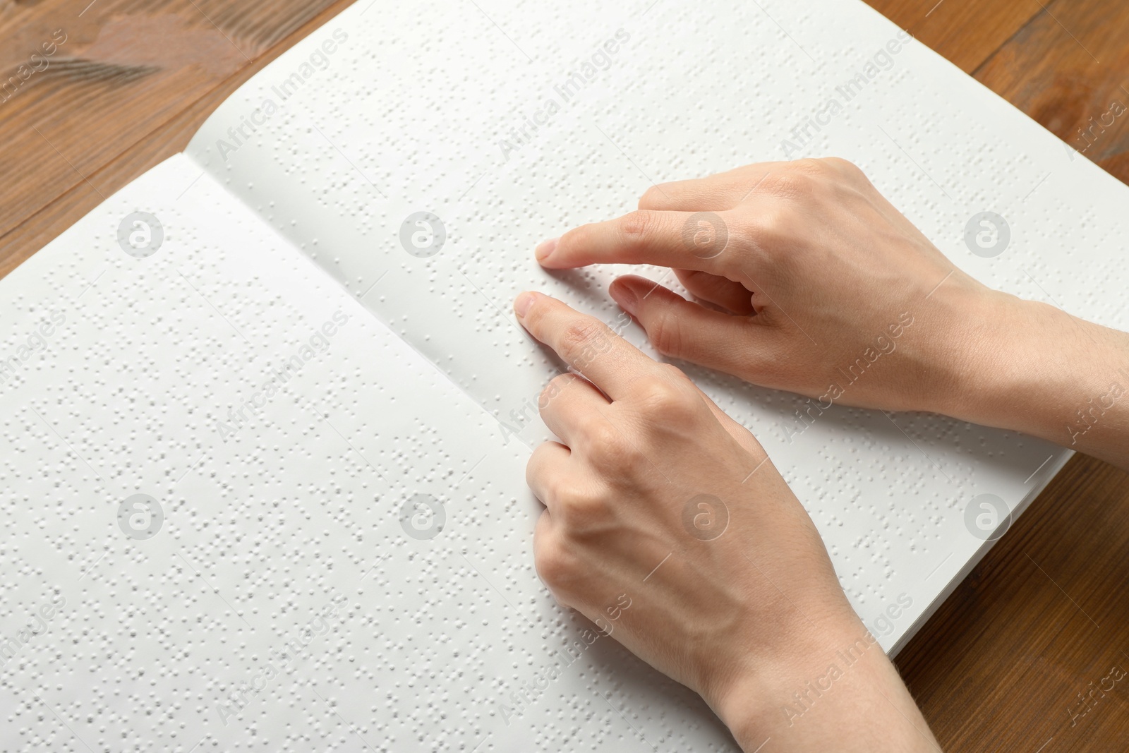 Photo of Blind woman reading book written in Braille at wooden table, closeup