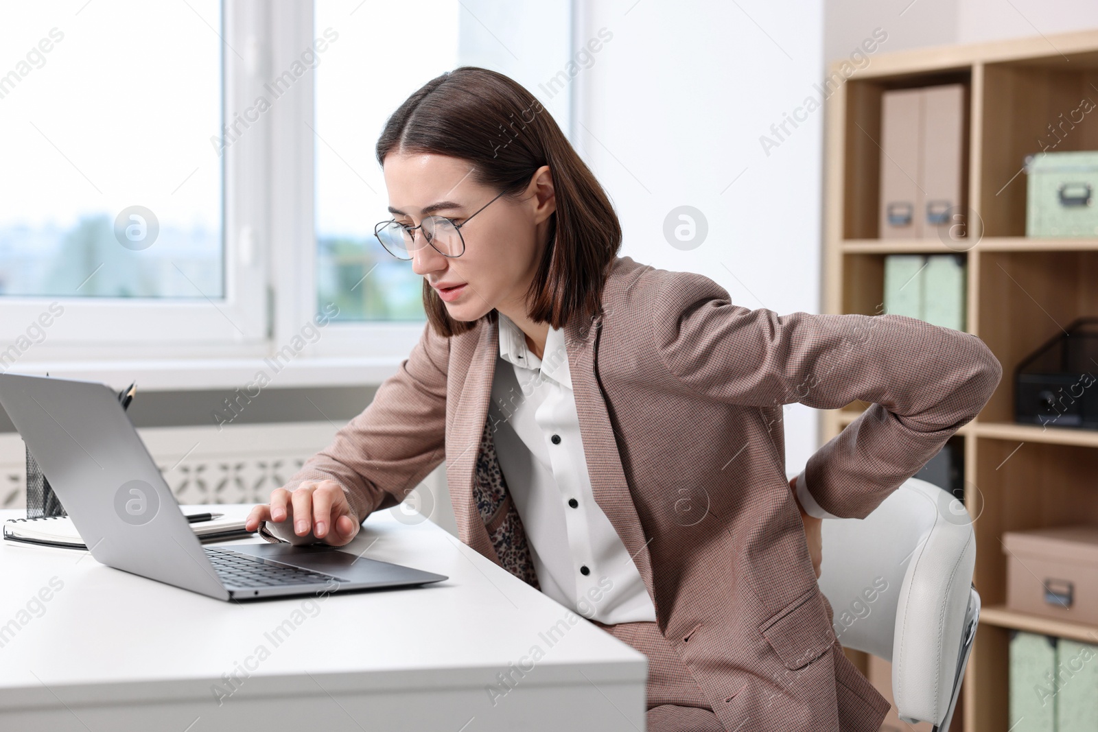 Photo of Woman suffering from back pain in office. Symptom of poor posture