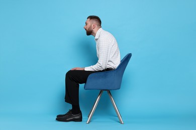 Photo of Man with poor posture sitting on chair against light blue background